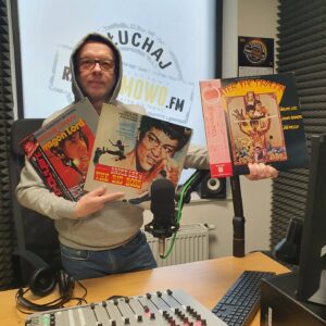 prowadzący audycję stoi za konsolą radiową z płytami winylowymi w rękach